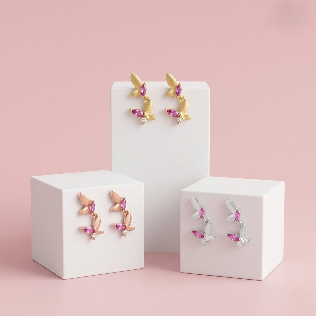 Three pairs of earrings on white stands against a pink background